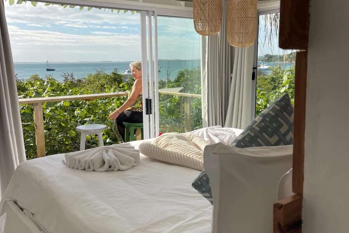 Bedroom with a large window overlooking the ocean and a guest relaxing on the balcony
